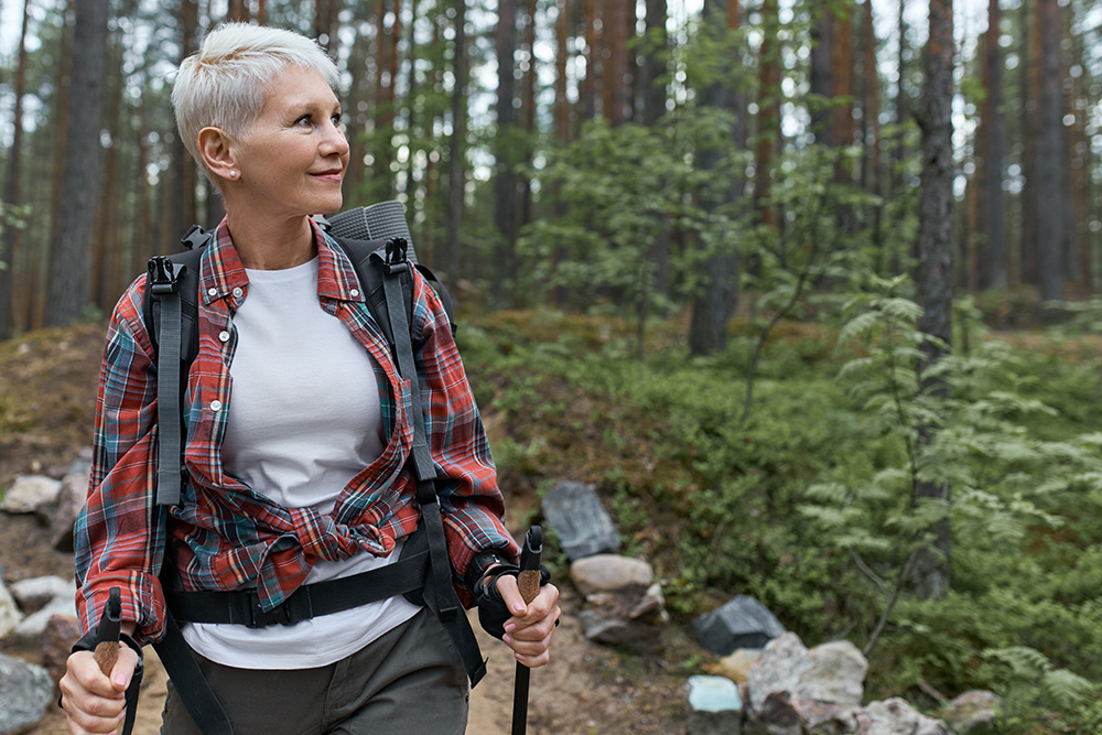 Senior woman hikes in woods after recovering from hip replacement surgery.